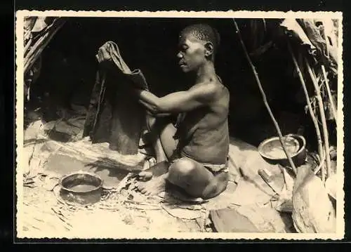 AK Eine afrikanische Frau bearbeitet in ihrer Hütte ein Stück Stoff