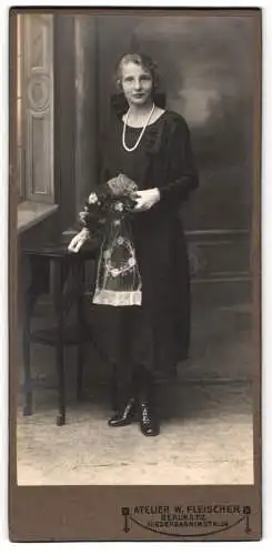 Fotografie W. Fischer, Berlin, Niederbarnimstr. 24, Junge Dame Frida im schwarzen Kleid mit Perlenkette und Blumenstrauss