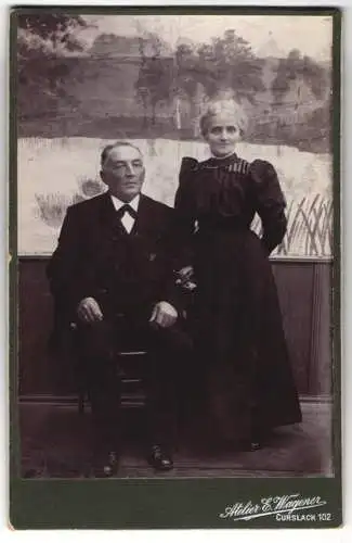 Fotografie E. WAgener, Curslack, Onkel Heinrich und Tante Anna in schwarzer eleganter Kleidung vor einer Studiokulisse