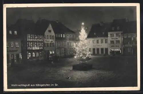 AK Königshofen im Gr., Marktplatz mit beleuchtetem Weihnachtsbaum und Geschäften aus der Vogelschau