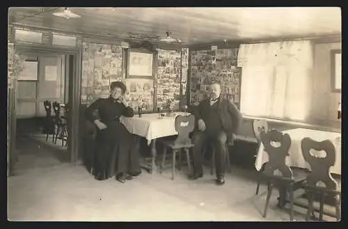 AK Paar in einem Gasthaus vor einer Wand mit Ansichtskarten, Ansichtskartengeschichte