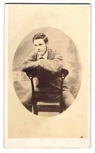 Fotografie W. Wort, Oscott, Junger Herr im Anzug sitzt rückwärts auf einem Stuhl