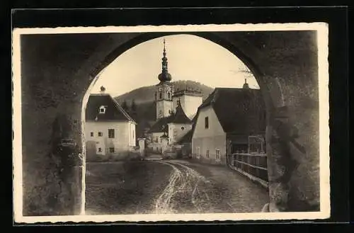 AK Heiligenkreuz /N.-D., Strassenpartie mit Kirche durch Tor gesehen