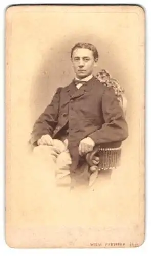 Fotografie Wilh. Pfeiffer, Reichenberg, Junger Mann im Anzug mit pomadisiertem Haar auf einem gepolsterten Stuhl