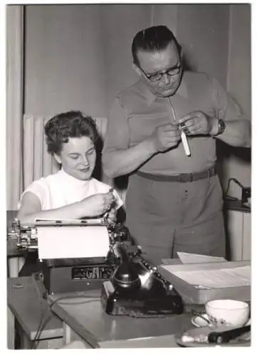 Fotografie Sekretärin nebst Schreibmaschine beim Uhrenvergleich mit dem Chef
