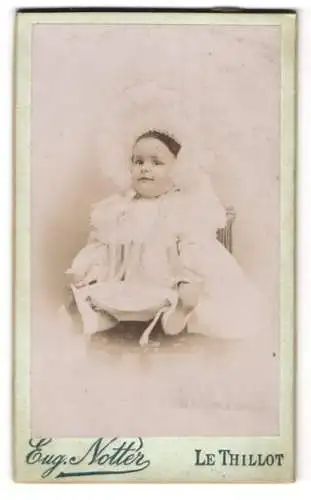 Fotografie Eug. Notter, Le Thillot, Lächelndes Baby im Kleidchen mit opulenter Haube