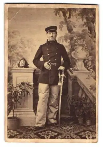 Fotografie unbekannter Fotograf und Ort, Feuerwehrmann in Uniform mit Säbel nebst Feuerwehr Helm, 1875