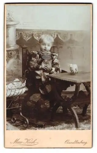 Fotografie Max Koch, Quedlinburg, niedliches kleines Kind im Kleid mit Babybett vor einer Studiokulisse