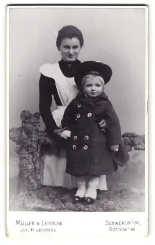 Fotografie Müller & Lembcke, Schwerin i. M., junge Amme / Kindermädchen mit ihrem Schützling im Mantel