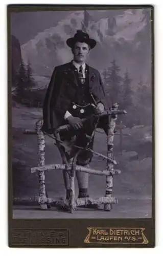 Fotografie Karl Dietrich, Laufen / Salzach, Herr in bayerischer Tracht mit Pfeife vor einer Studiokulisse