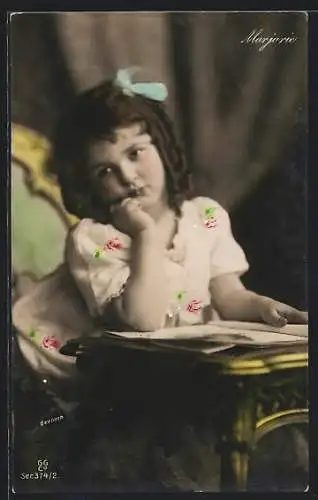 Foto-AK GG Co. Nr. 374 /2: Die kleine Marjorie sitzt gelangweilt mit einem Heft am Tisch