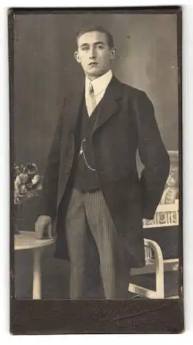 Fotografie Carl Walther, Wilhelmshaven, Junger schöner Herr im schwarzen Anzug mit Taschenuhr und heller Krawatte