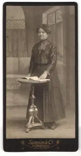 Fotografie Samson & Co., München, Neuhauserstr. 7, Junge schöne Dame im schwarzen Kleid mit Brosche und offenem Buch