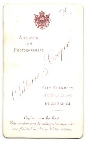 Fotografie Oldham & Cooper, Birmingham, 82 New Street, Niedliches Kind im weiss-schwarzen Kleid schmollt auf einem Kissen