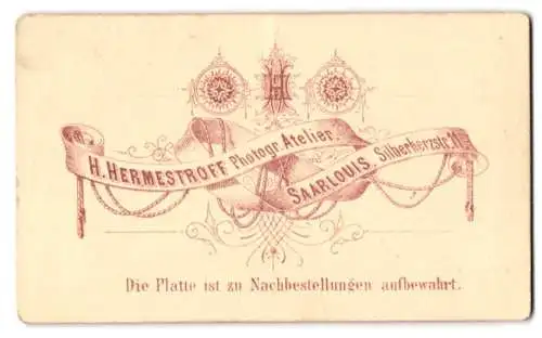 Fotografie H. Hermestroff, Saarlouis, Silberherzstr. 11, Monogramm des Fotografen über Banderole mit Anschrift