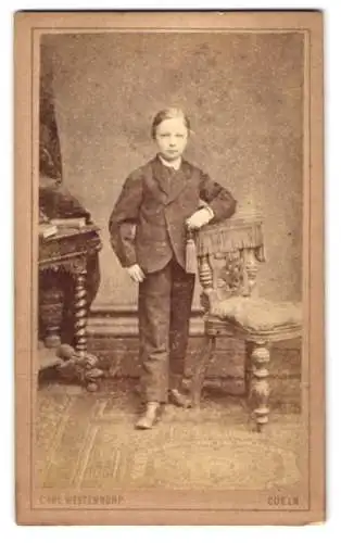 Fotografie Carl Westendorp, Coeln a. Rh., Comödien-Str. 7, junger Knabe im Anzug lehnt an einem Stuhl