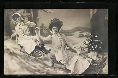 AK ZWei Frauen auf Schlitten, posierend, Häuser und Wald im Hintergrund