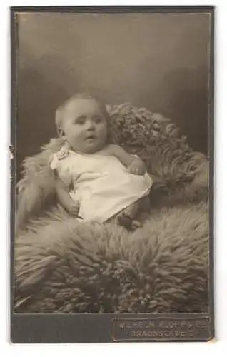 Fotografie Wilhelm Klopp & Co., Braunschweig, Süsses Kleinkind im Hemd liegt auf einem Fell