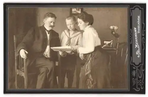 Fotografie Ad. Behrmann, Visselhövede, Vater und Mutter zeigen ihrem Sohn etwas in der Zeitung