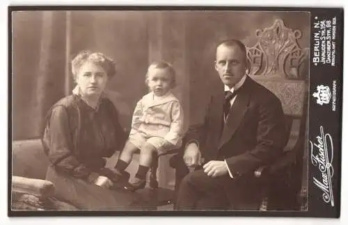 Fotografie Max Fischer, Berlin, Invaliden Str. 164, Junge Familie in dunkler Kleidung mit Kleinkind im weissen Hemd