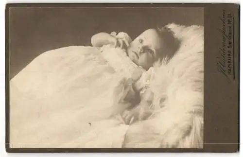 Fotografie J. Waldemar Jacobsen, Hamburg, Steindamm 51, Niedliches Baby im weissen Kleid mit dunklen Haaren auf Fell