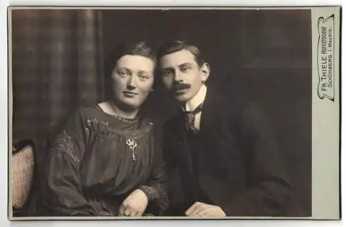Fotografie Fr. Thiele, Schönberg, Junges elegantes Paar in schwarzer Kleidung, Herr mit Schnurrbart und Dame mit Brosche