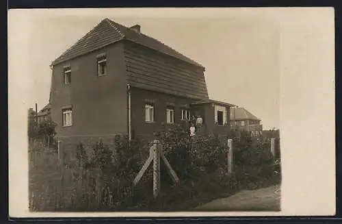 Foto-AK Döbern /Lausitz, Neusiedler-Haus mit Bewohnern im Eingang, von der Strasse gesehen