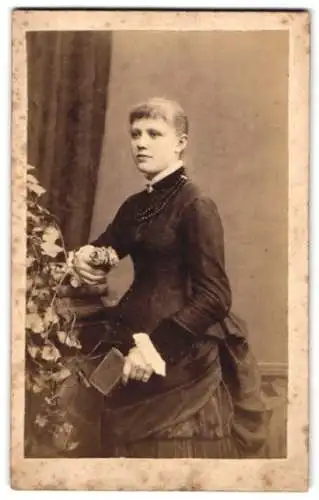 Fotografie J. F. Petersen, Lübeck, Obere Aegidienstr. 8, Junge Frau im taillierten Kleid mit einem Buch in der Hand