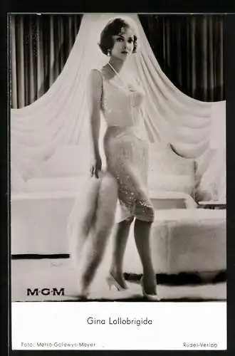 AK Schauspielerin Gina Lollobrigida im weissen Kleid mit Pelz vor einem Bett