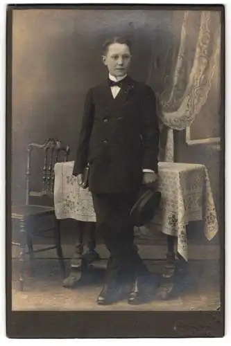 Fotografie Wilh. Schrörs, Lemgo, Junge mit Buch und Schiebermütze in den Händen