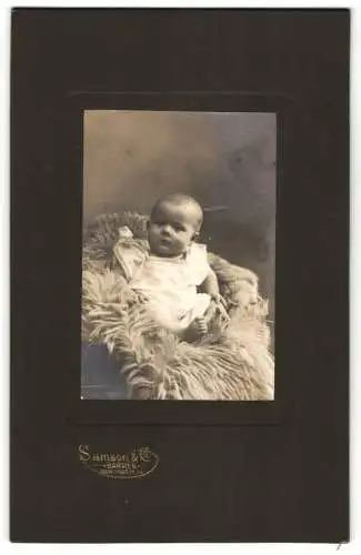 Fotografie Samson & Co., Berlin, Wertherstrasse 13, Baby im weissen Strampelkleid auf einem Fell