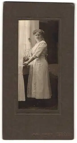 Fotografie Max Holdt, Pirna /A. E., Garten-Str. 31, Junge Dame mit ondulierten Haaren im weissen Kleid an einem Fenster