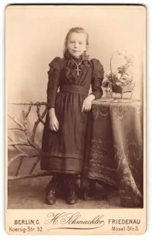 Fotografie H. Schmuckler, Friedenau, Mosel-Str. 3, Lächelndes Mädchen mit Kreuzkette an Tisch gelehnt