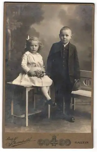 Fotografie Rudolf Schandalik, Hallein, Zwei niedliche junge Geschwister in feiner Kleidung mit Hut und Puppe