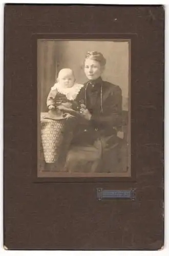 Fotografie Diedr. Kassens, Delmenhorst-Vechta, Junge Mutter im schwarzen Kleid mit niedlichem Baby im Arm