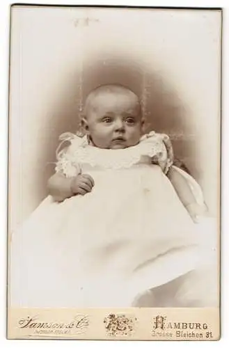 Fotografie Samson & Co, Hamburg, Grosse Bleichen 31, Niedliches Baby im weissen Kleid mit Spitze und Paustbacken