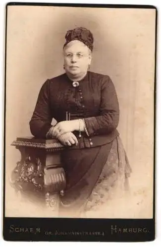 Fotografie Schaem, Hamburg, Gr. Johannisstr. 4, Gutbürgerliche Dame im schwarzen Kleid mit Kopfbedeckung und Brosche