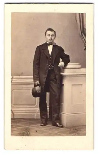 Fotografie F. Grill, Hanau, junger Mann im Anzug mit Fliege und Hut in der Hand, geprägter Trockenstempel