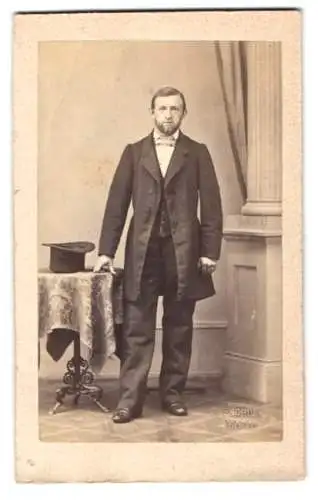 Fotografie F. Grill, Hanau, Herr im Anzug mit Vollbart nebst Zylinder auf dem Tisch, geprägter Trockenstempel