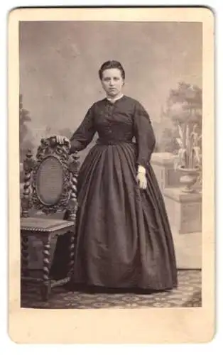 Fotografie A. Breuning, Hanau, junge Frau im dunklen Kleid vor einer Studiokulisse