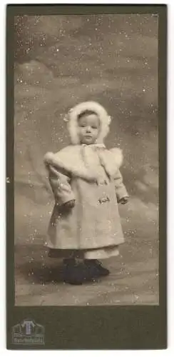 Fotografie Hermann Tietz, München, niedliches kleines Mädchen im Wintermantel mit Kapuze, Montage mit Schnee im Studio