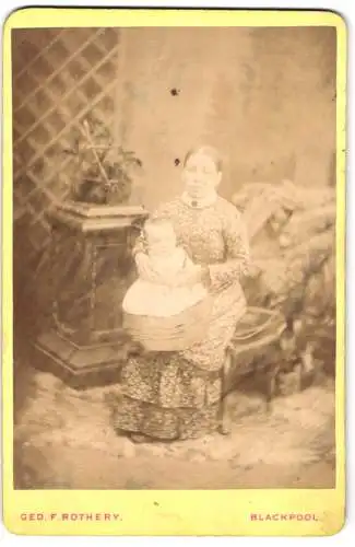 Fotografie Geo F. Rothery, Blackpool, Dame in geblümtem Kleid mit Kleinkind auf dem Schoss