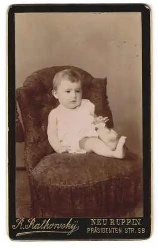 Fotografie R. Ratkonsky, Neuruppin, Präsidentenstr. 58, Kleinkind im weissen Gewand auf einem Sessel