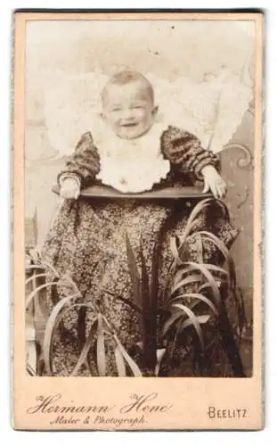 Fotografie Hermann Hene, Beelitz, Kleinkind im langen floral-gemusterten Kleid mit Latz im Kinderstuhl