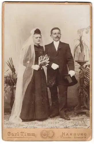 Fotografie Carl Timm, Harburg / Elbe, junges Brautpaar im dunklen Hochzeitskleid und Anzug mit Zylinder