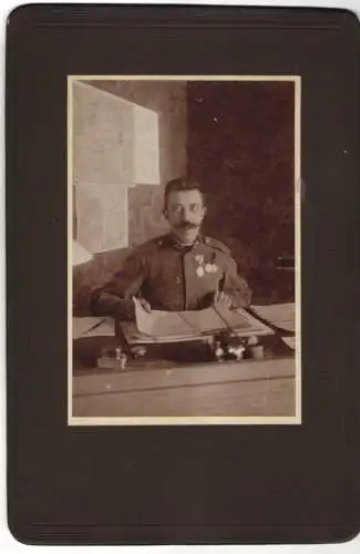Fotografie unbekannter Fotograf und Ort, K.u.K. Soldat in Uniform mit Orden an der Brust in seiner Schreibstube