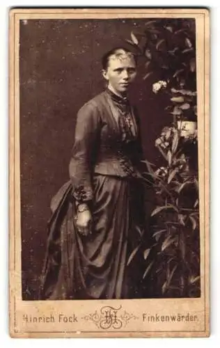 Fotografie Hinrich Fock, Finkenwärder, Junge Dame in elegantem Kleid neben Rosenstrauch