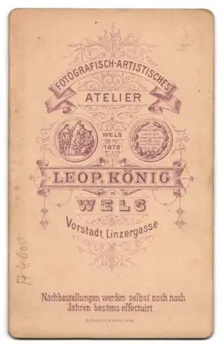 Fotografie Leopold König, Wels, Linzergasse, Ein Mann mit verschränkten Armen neben einem Tisch mit Uhr