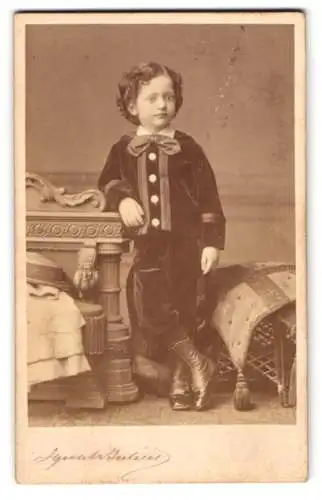 Fotografie Ignatz Julius, Hamburg, Grosse Bleichen 31, Kleiner Junge in elegantem Outfit lehnt an Möbelstück