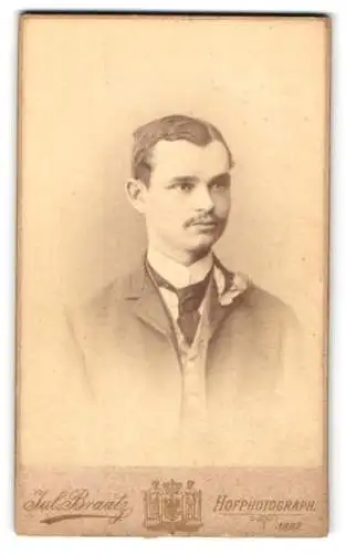 Fotografie Jul Braatz, Stettin, Am Königs Thor 13, Portrait eines jungen Mannes im Anzug mit Blumendekoration